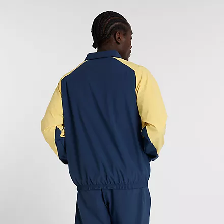 Rückansicht einer New Balance In Game Woven Track Jacket in Navy mit gelben Ärmeln an einem Mann.