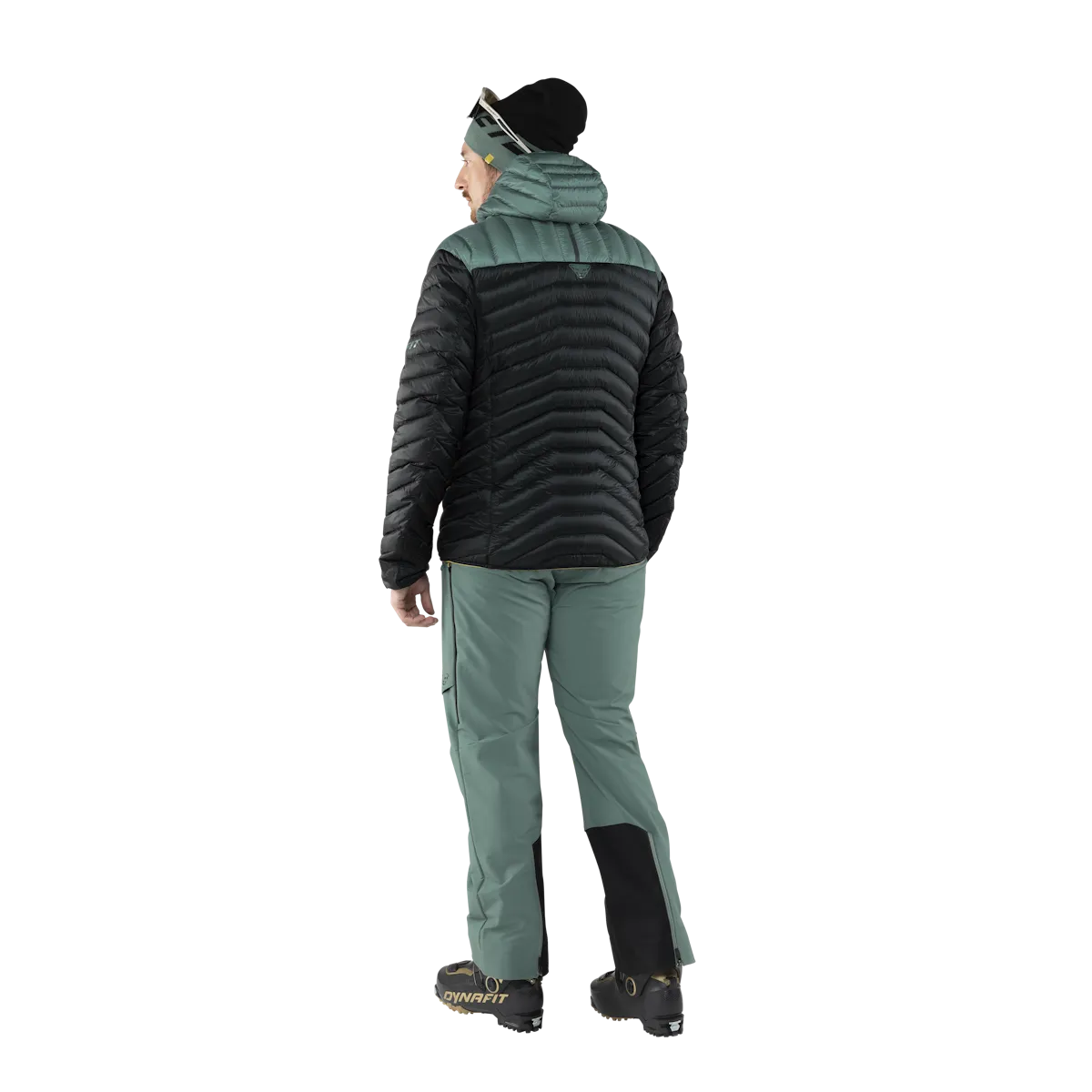 Rückansicht: Person mit Dynafit Ridge Ultralight Daunenjacke in Schwarz und Grün. Ski-Hose, Mütze und Skischuhe.