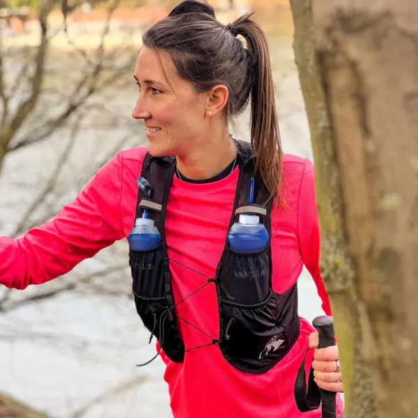 Läuferin mit Trinkweste Hydrabag Elite 8L und zwei blauen Trinkflaschen. Sie hält einen Trekkingstock in der Hand.