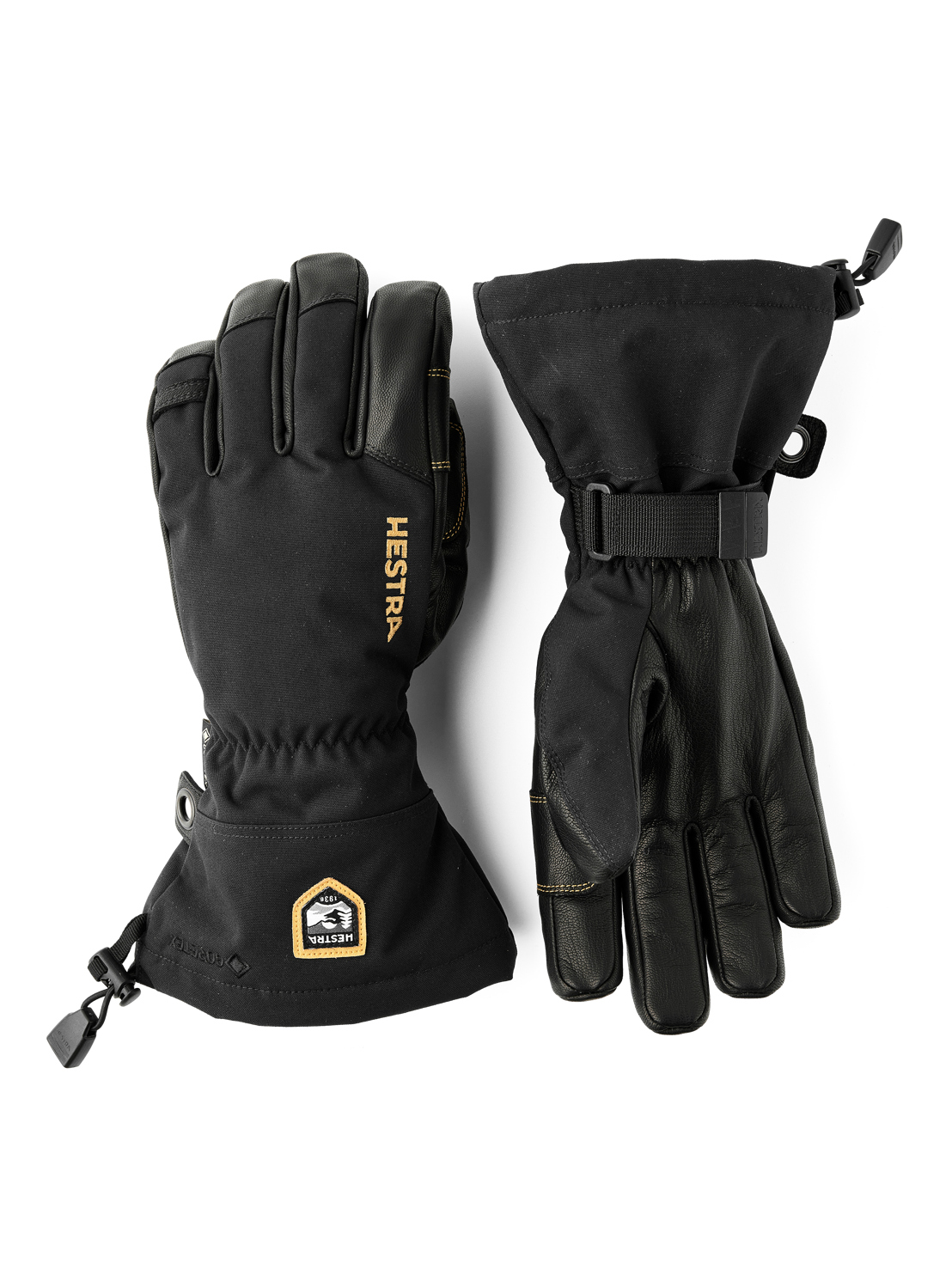 Zwei schwarze Hestra Gore-Tex 5-Finger-Handschuhe liegen auf einer weißen Oberfläche. Einer hat ein Hestra-Logo.