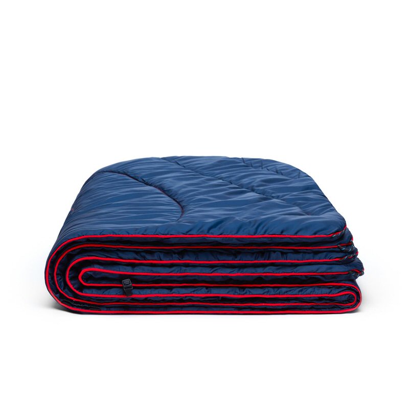Zusammengefaltete, gesteppte, dunkelblaue Rumpl Puffy Blanket mit roter Umrandung auf weißem Hintergrund.