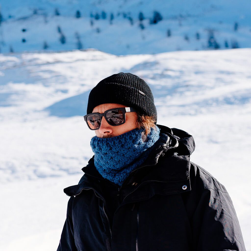 Mann im Schnee Mann mit Mütze, Sonnenbrille und blauem Stroller Neckwarmer im Schnee.