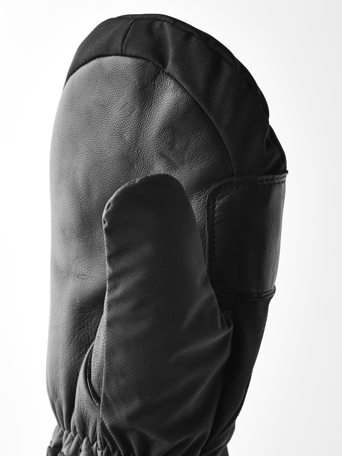 Schwarzer Lederfäustling Schwarzer Lederfäustling mit Daumen, Manschette aus Stoff und geripptem Handgelenksabschluss, vor weißem Hintergrund.