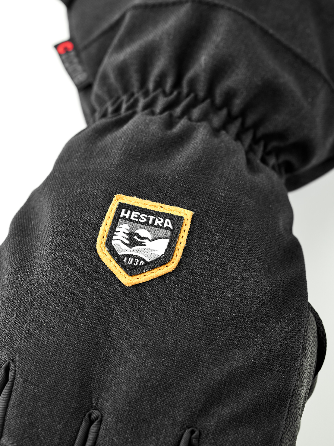 Detailansicht eines schwarzen Handschuhs mit Hestra-Logo, das Berge und das Gründungsjahr 1936 zeigt.