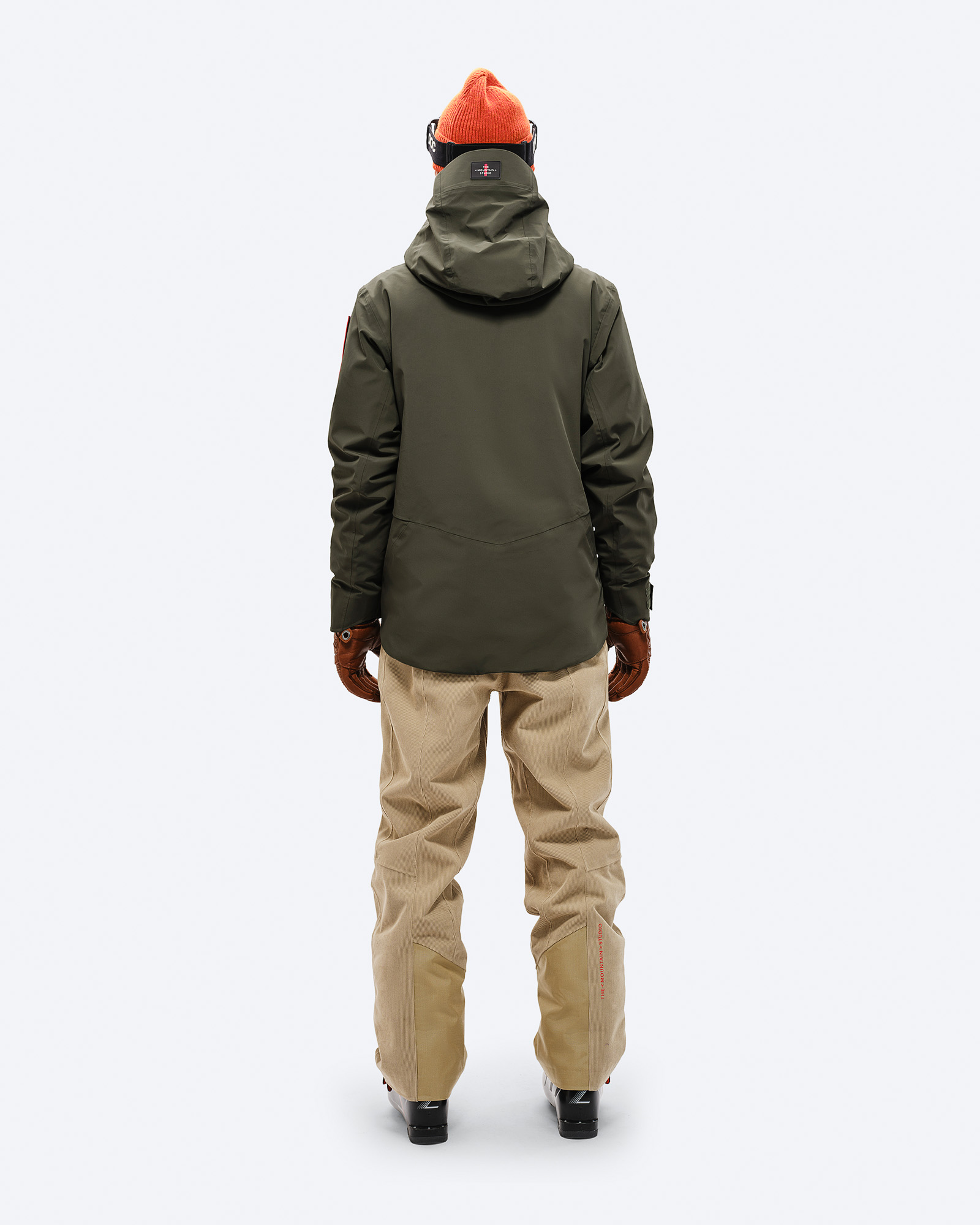 Rückenansicht einer Person in Forest Green S-3 Carv Insulated Stretch Jacket mit Skibrille, Mütze, Handschuhen, Hose und Skischuhen.