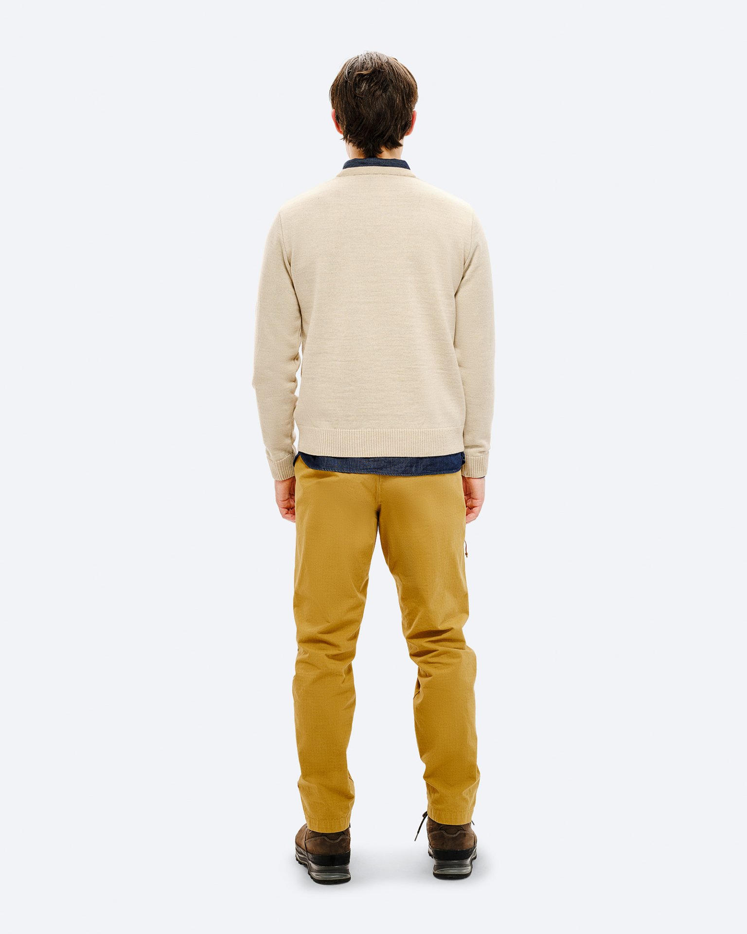 Rückansicht eines Mannes mit beigem Ski Sweater, gelben Hosen und braunen Schuhen vor neutralem Hintergrund.