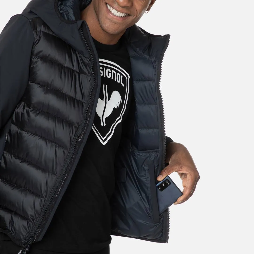 Mann trägt Rossignol Stretch Quilt Hoodie JKT in Schwarz. Hand steckt Smartphone in die Jackentasche.