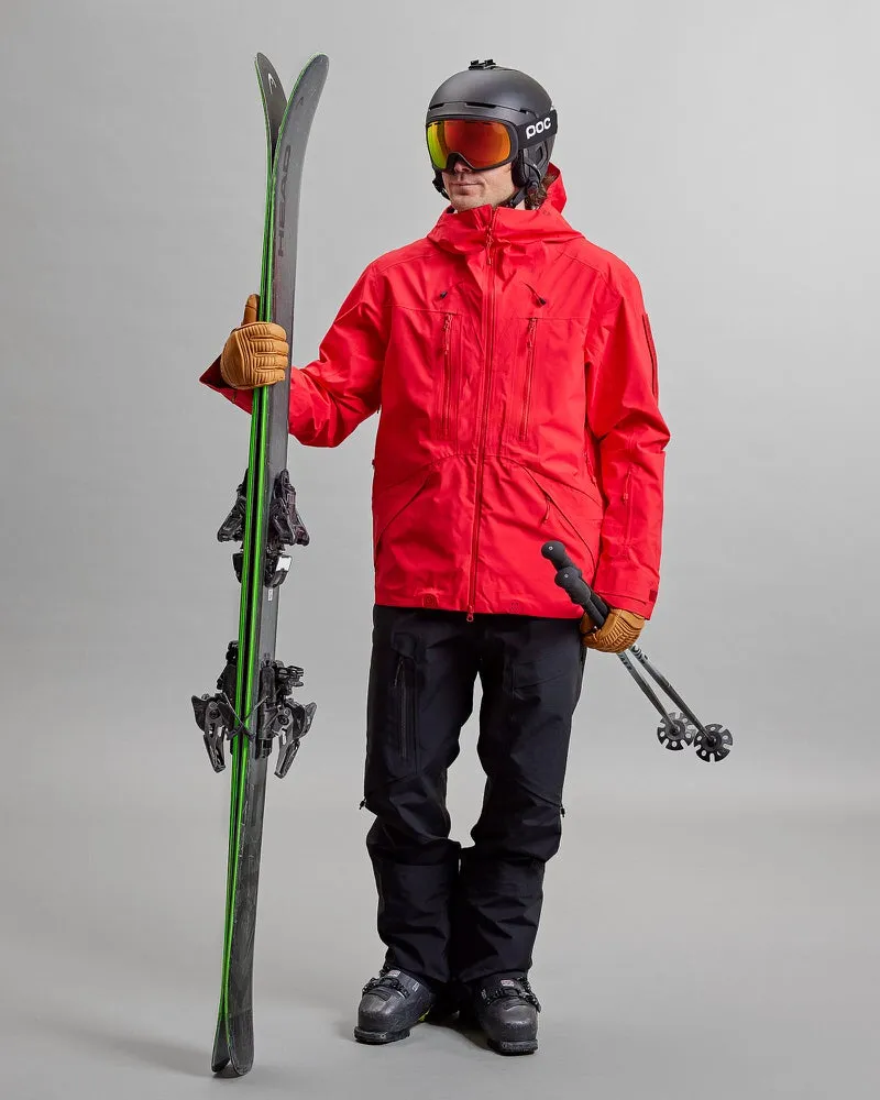 Person in Skikleidung, rote Jacke, schwarze Y-1 HD GORE-TEX Pro Hose, Helm, Skibrille, Skier und Stöcke.