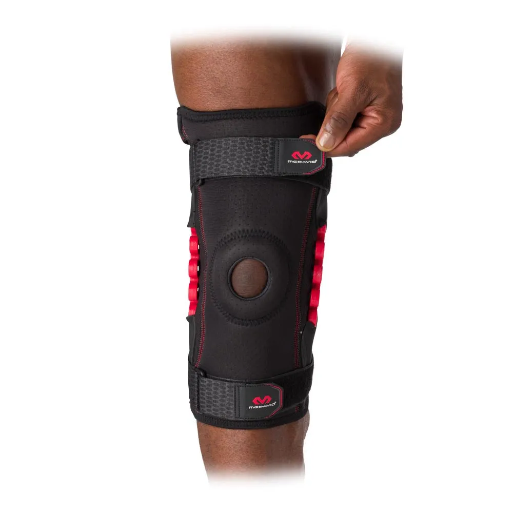 Nahaufnahme einer schwarzen McDavid NRG Knee Brace am Knie, mit rotem Gelenk und Hand an einem Riemen.