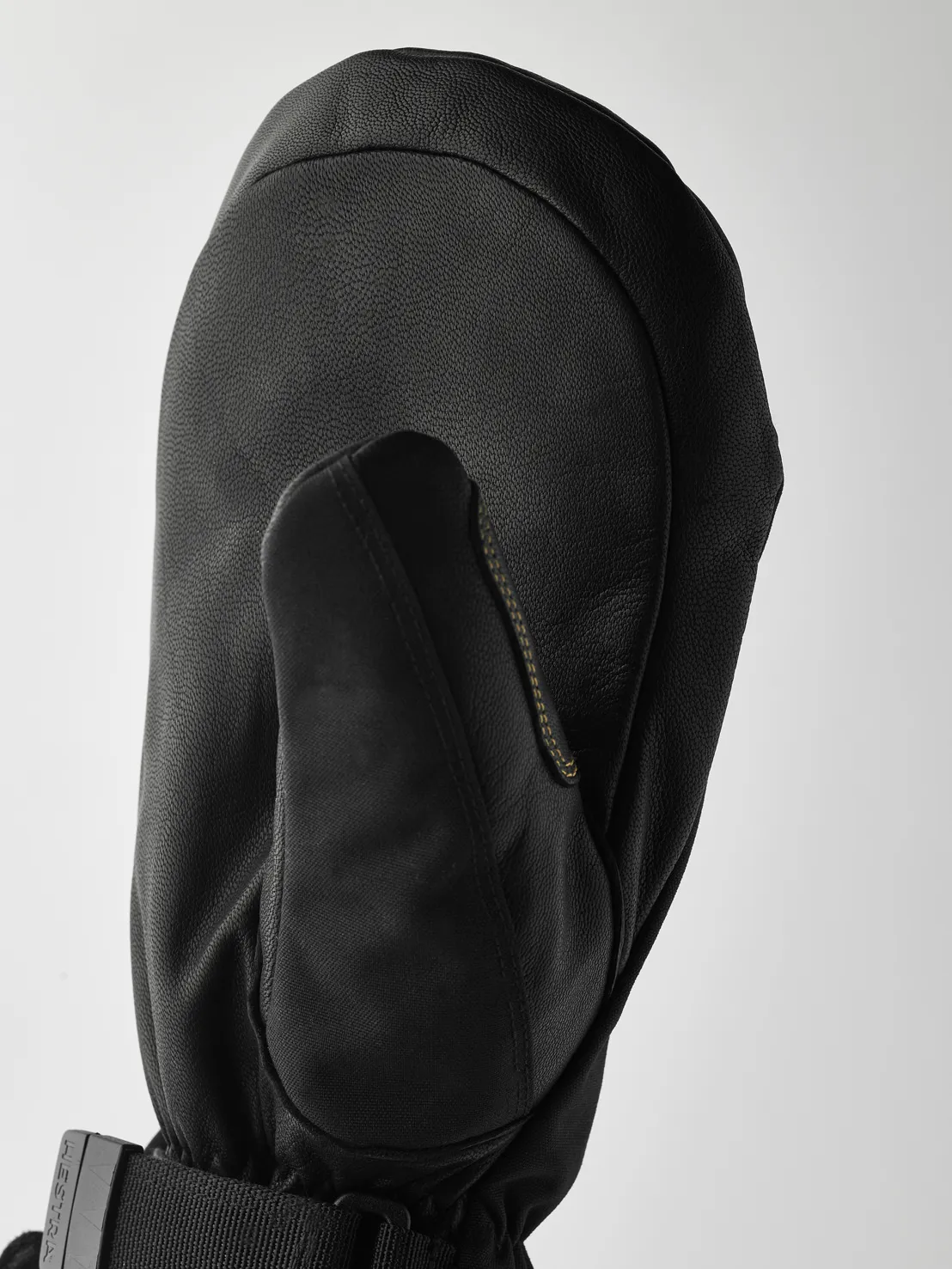 Detailaufnahme eines schwarzen Lederhandschuhs mit Daumen, Manschette mit Band und Schnalle vor hellem Hintergrund.
