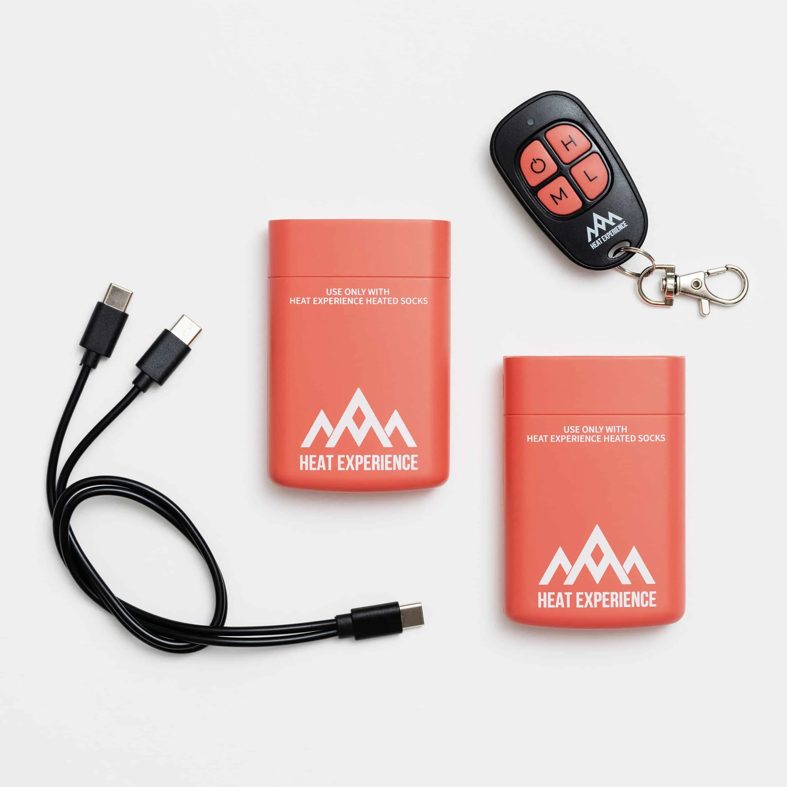 Zwei Akkus, USB-Kabel und Fernbedienung für Heat Experience beheizbare Skisocken auf weißem Grund.