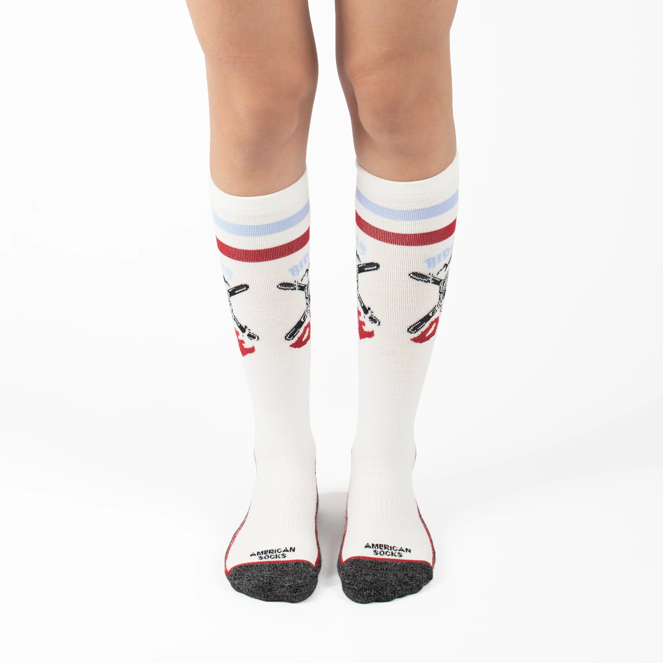 Beine mit kniehohen, weißen Snow Socks, Design mit gekreuzten Snowboards und roten/blauen Streifen. "Ride or Die" Schriftzug.