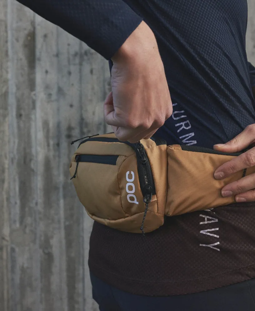 Person mit POC Lamina Hüfttasche in Aragonite Brown. Die Tasche hat Fächer und Reißverschlüsse.