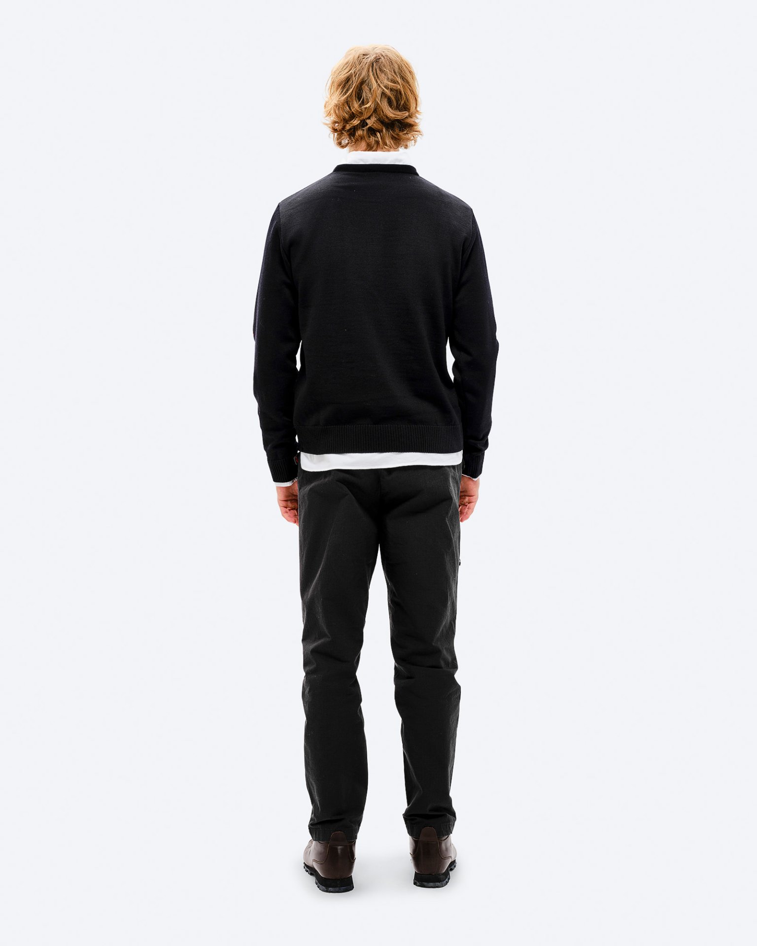 Rückenansicht eines Mannes mit blonden Haaren in schwarzem K-3 Ski Sweater, Hose und Schuhen vor weißem Hintergrund.