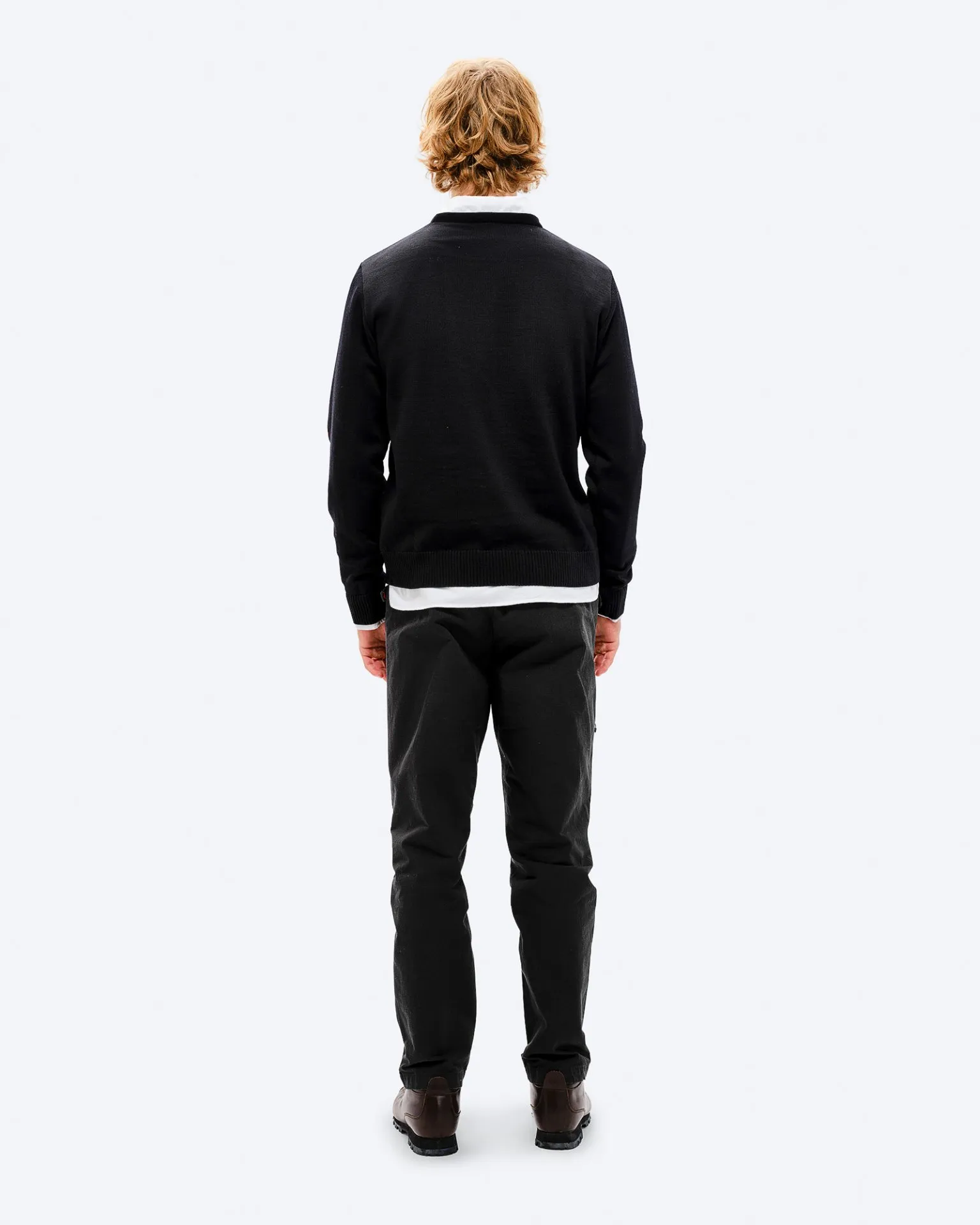 Rückenansicht eines Mannes mit blonden Haaren in schwarzem K-3 Ski Sweater, Hose und Schuhen vor weißem Hintergrund.