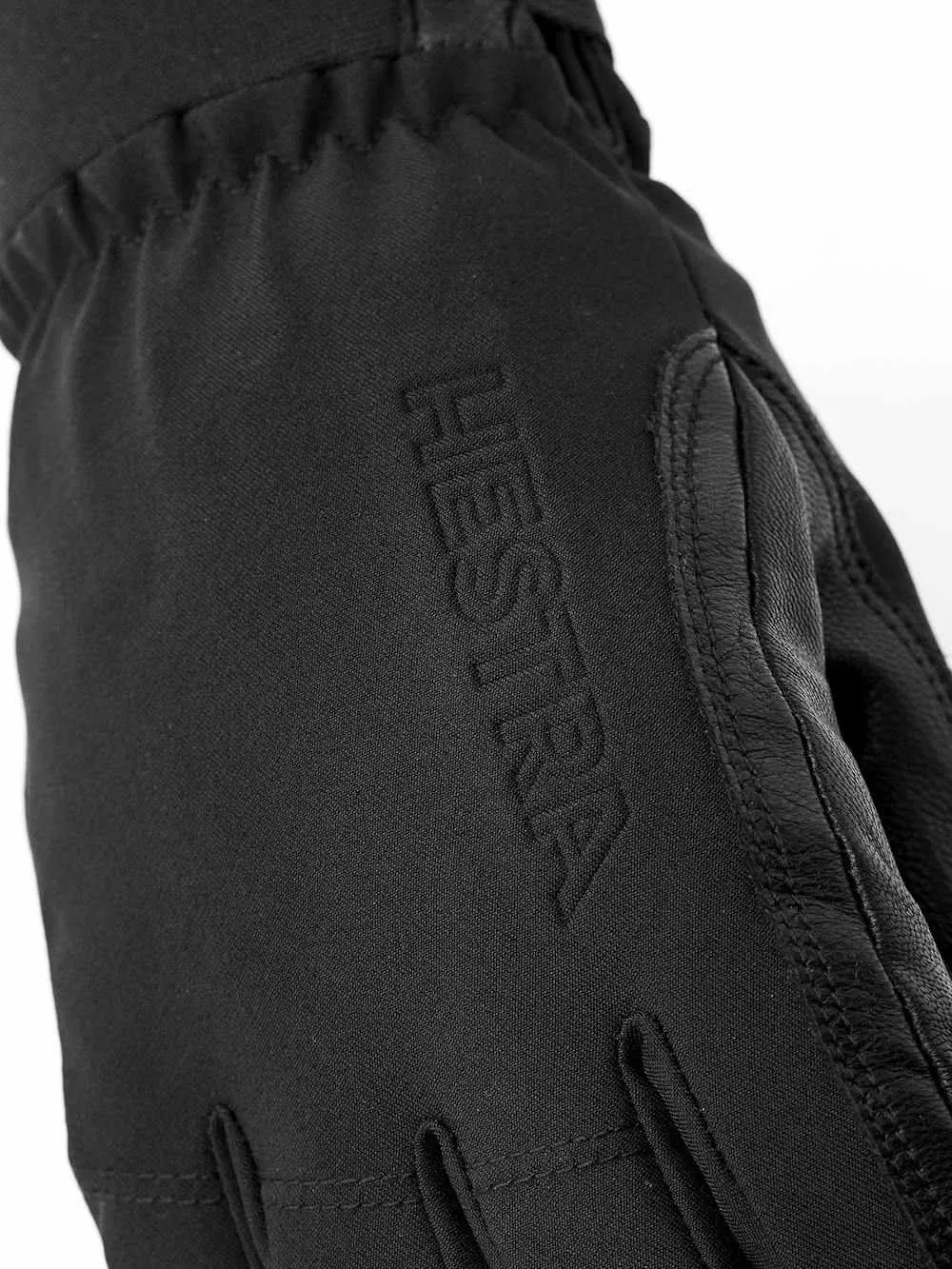 Nahaufnahme eines schwarzen Hestra-Handschuhs mit Lederdetails und eingeprägtem Markennamen.