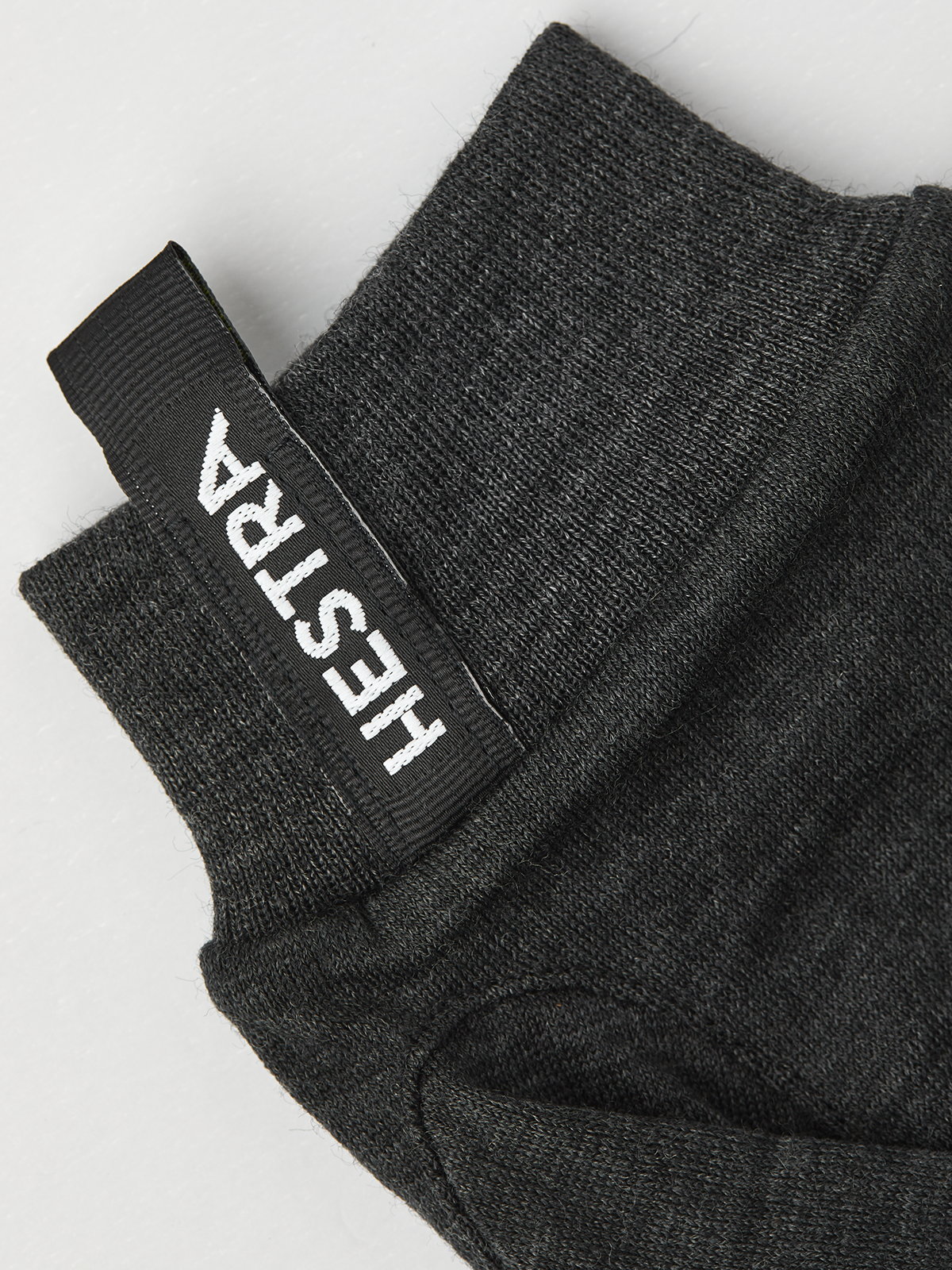 Nahaufnahme eines grauen Merino Wool Liner Active Handschuhs mit dem Hestra-Logo am Bündchen.