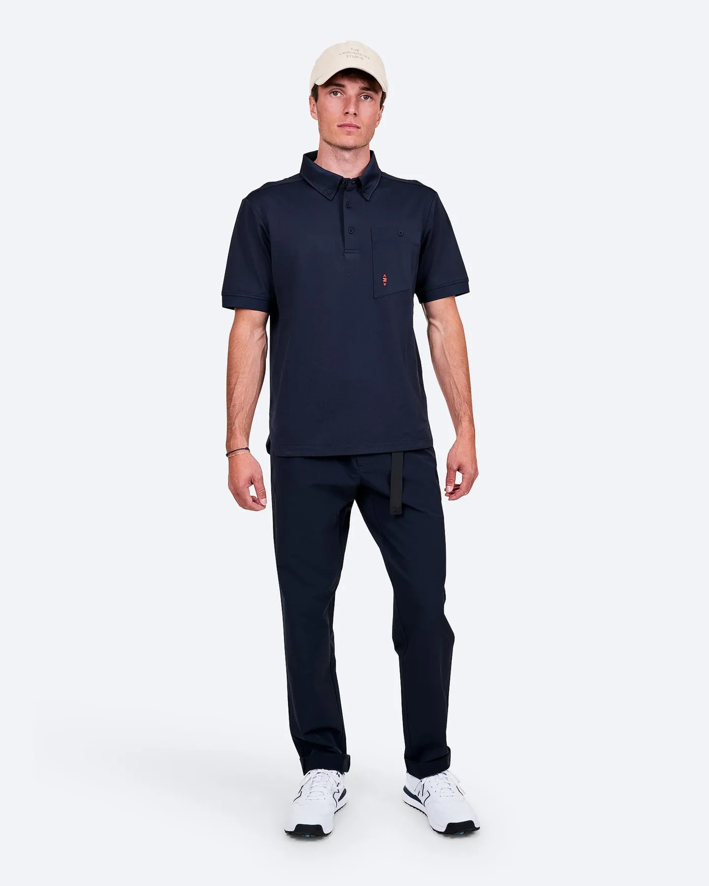 Ein Mann in Marineblauem Polohemd, Hose und weißem Cap steht auf einem weißen Hintergrund.