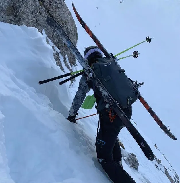 Person mit Salewa Randonee Rucksack und Skiern auf dem Rücken, beim Aufstieg im Schnee.
