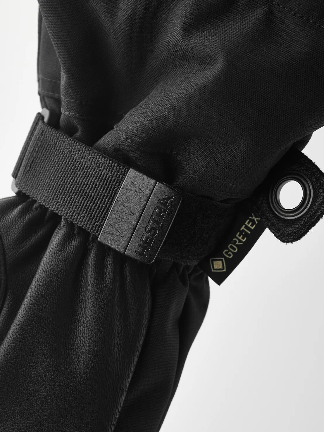 Detailaufnahme eines schwarzen Hestra Army Leather Gore-Tex Fäustlings mit Riemen und Gore-Tex Etikett.