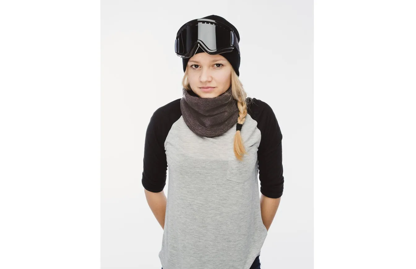 Junge Frau mit grauem Wellness Neckwarmer, Mütze und Skibrille vor weißem Hintergrund.