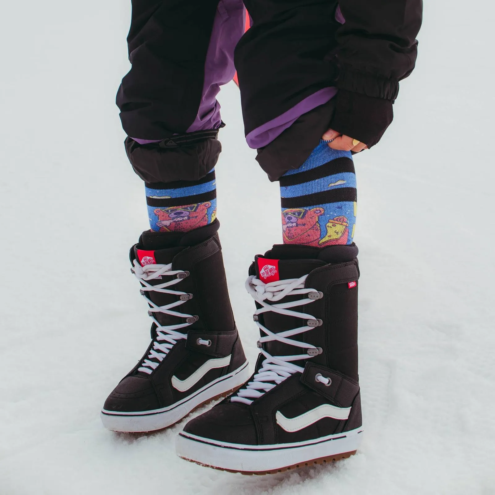 Person mit Snowboardstiefeln und Wild Nature Socken im Schnee. Socken mit Bärenmuster.