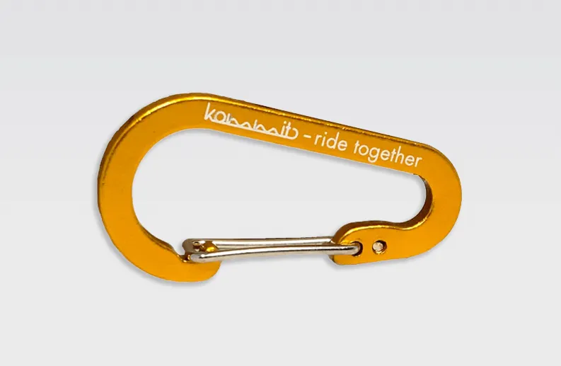 Detailansicht: Oranger kommit Karabiner mit silbernem Verschluss und weißer Aufschrift "kommit - ride together".