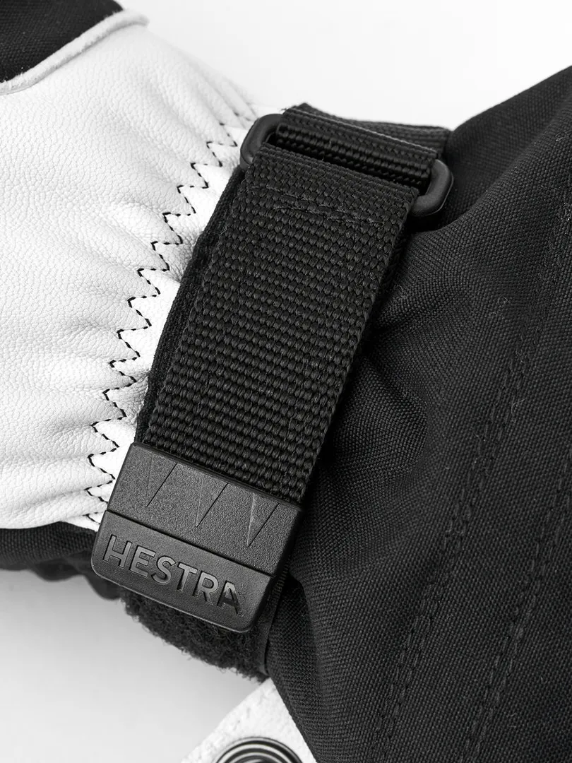 Detailaufnahme eines schwarzen Hestra Skihandschuhs mit weißem Lederteil und einem schwarzen Gurt mit dem Hestra-Logo.