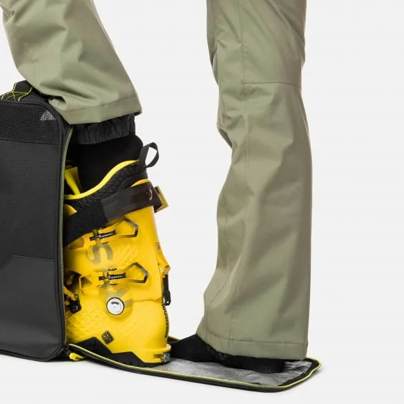 Gelber Skischuh wird in eine offene, schwarze Rossignol Soul Boot Bag gestellt. Person mit Hose steht daneben.