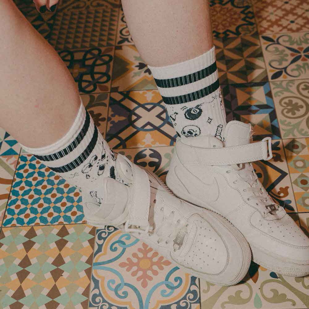 Beine mit "Flash Tattoo - Mid High" Socken und weißen Schuhen auf einem gemusterten Fliesenboden.