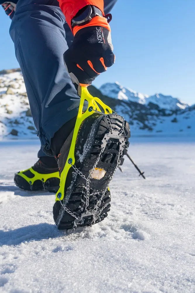 Schuhkralle am Schuh auf Schnee befestigt. Die Schuhkralle hat gelbe Elastomer und Steigeisenplatten.
