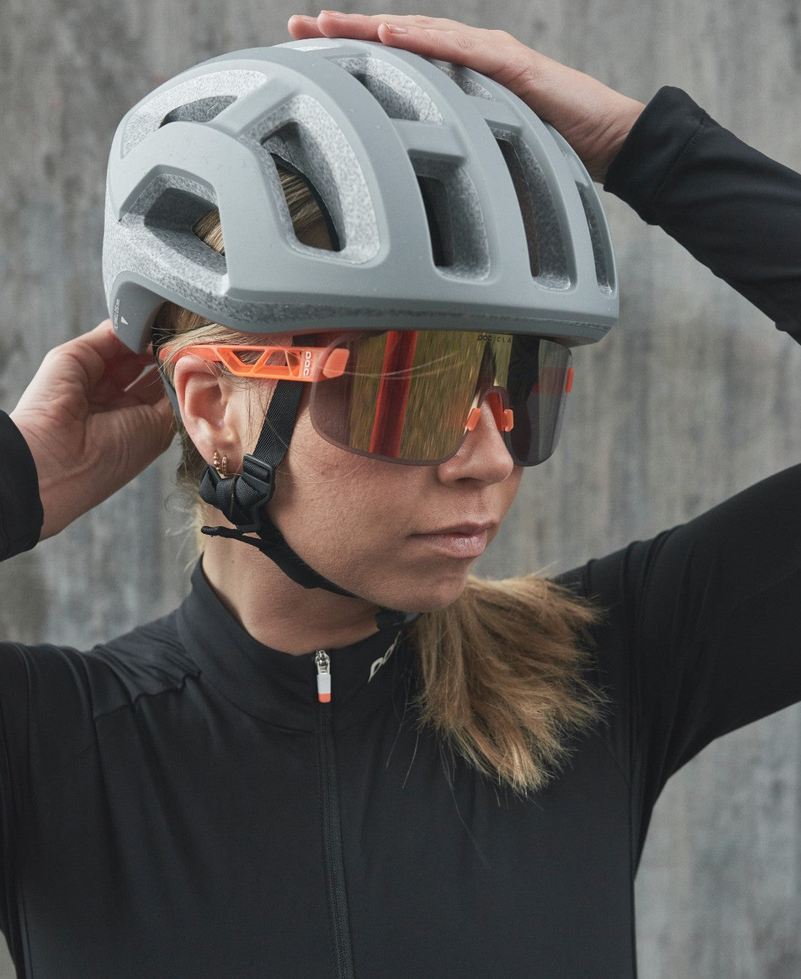 Fahrerin mit grauem Helm und orangefarbener POC Elicit Sonnenbrille mit Gold Mirror Glas.