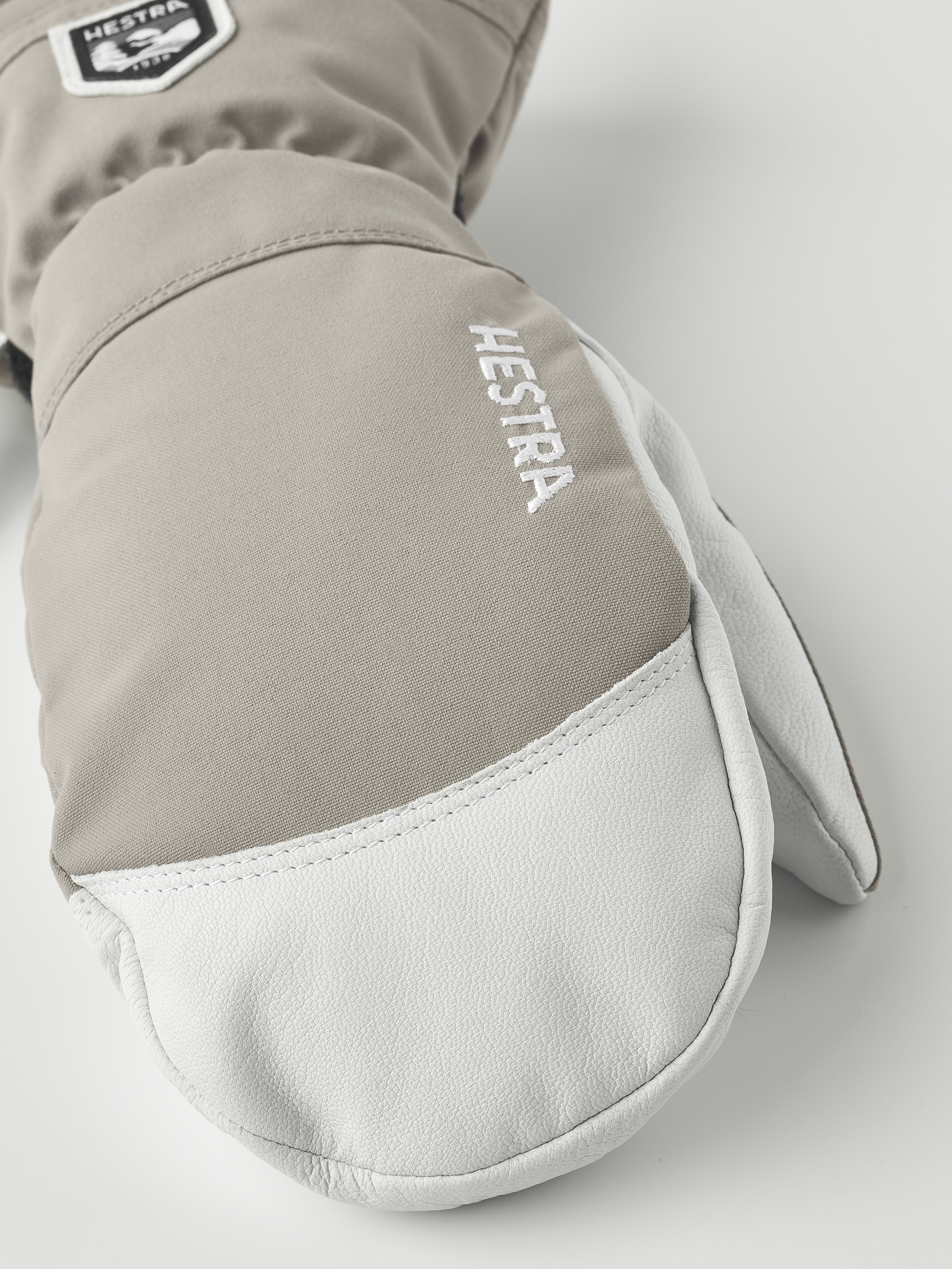 Nahaufnahme eines hellbraunen Hestra Army Leather Heli Ski Mitt Fausthandschuhs mit weißem Leder an der Spitze.