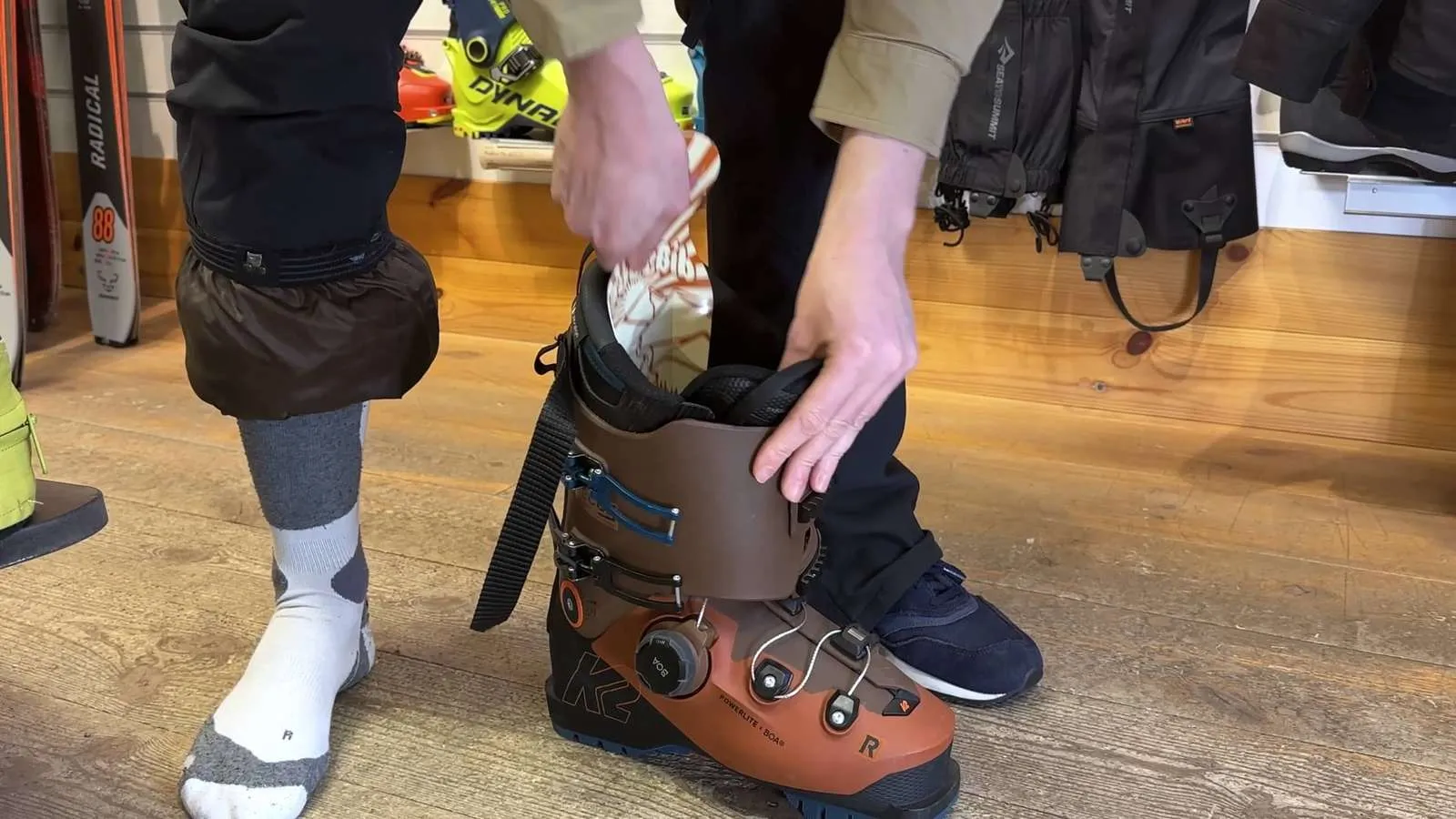 Person setzt einen Skischuh an. Brauner K2 Powerlite Skischuh mit Boa System wird angezogen. Socken und Gamaschen sind sichtbar.