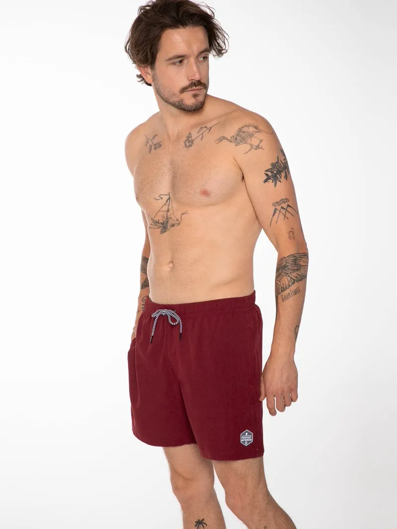 Mann mit Tätowierungen trägt rote "Protest Davey" Badeshorts mit Kordelzug.