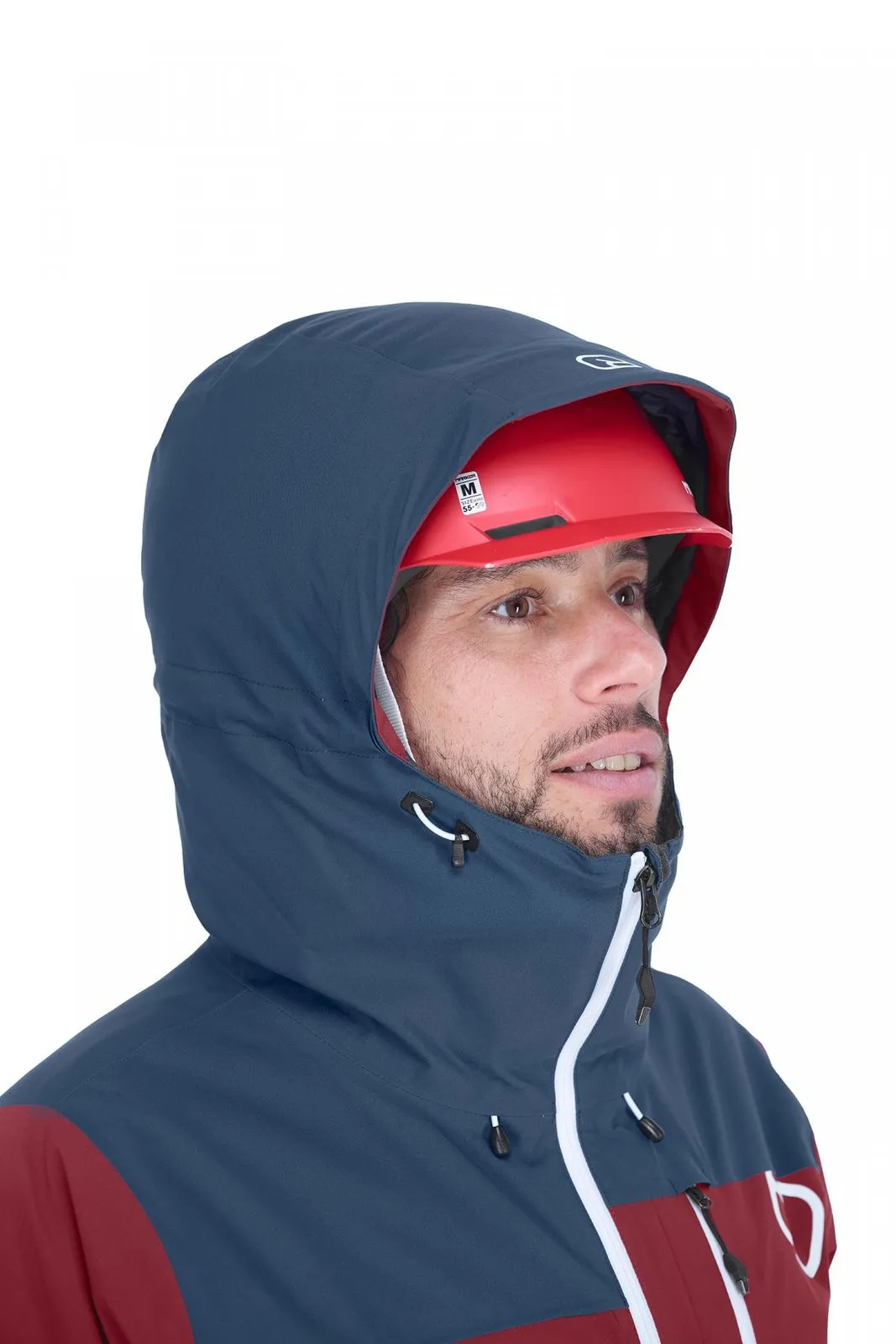 Mann mit rotem Helm trägt die blaue Ortovox Andermatt Jacke mit Kapuze, die teilweise das Gesicht verdeckt.