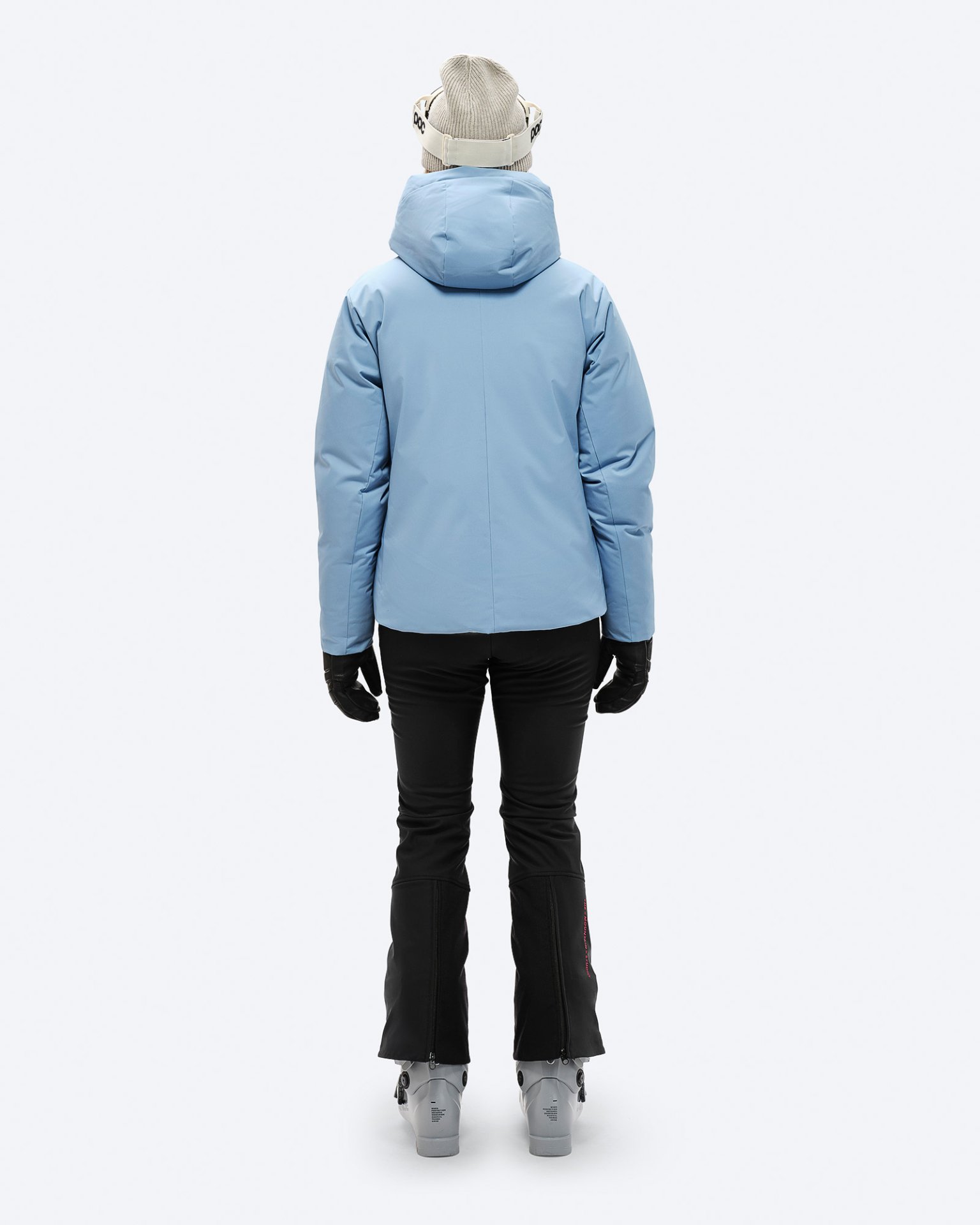 Rückansicht einer Person in blauer Daunenjacke mit Kapuze, Skihose, Handschuhen und Skischuhen.