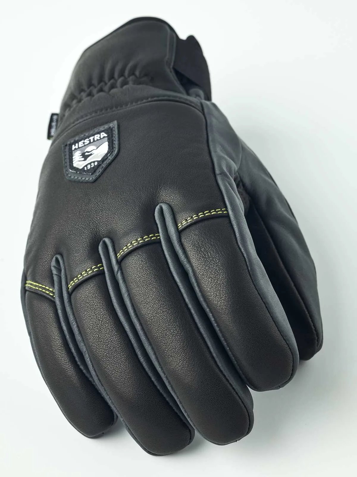Detailansicht des schwarzen Hestra Omni Trigger Handschuhs aus Leder mit Logo-Aufnäher und gelber Naht.