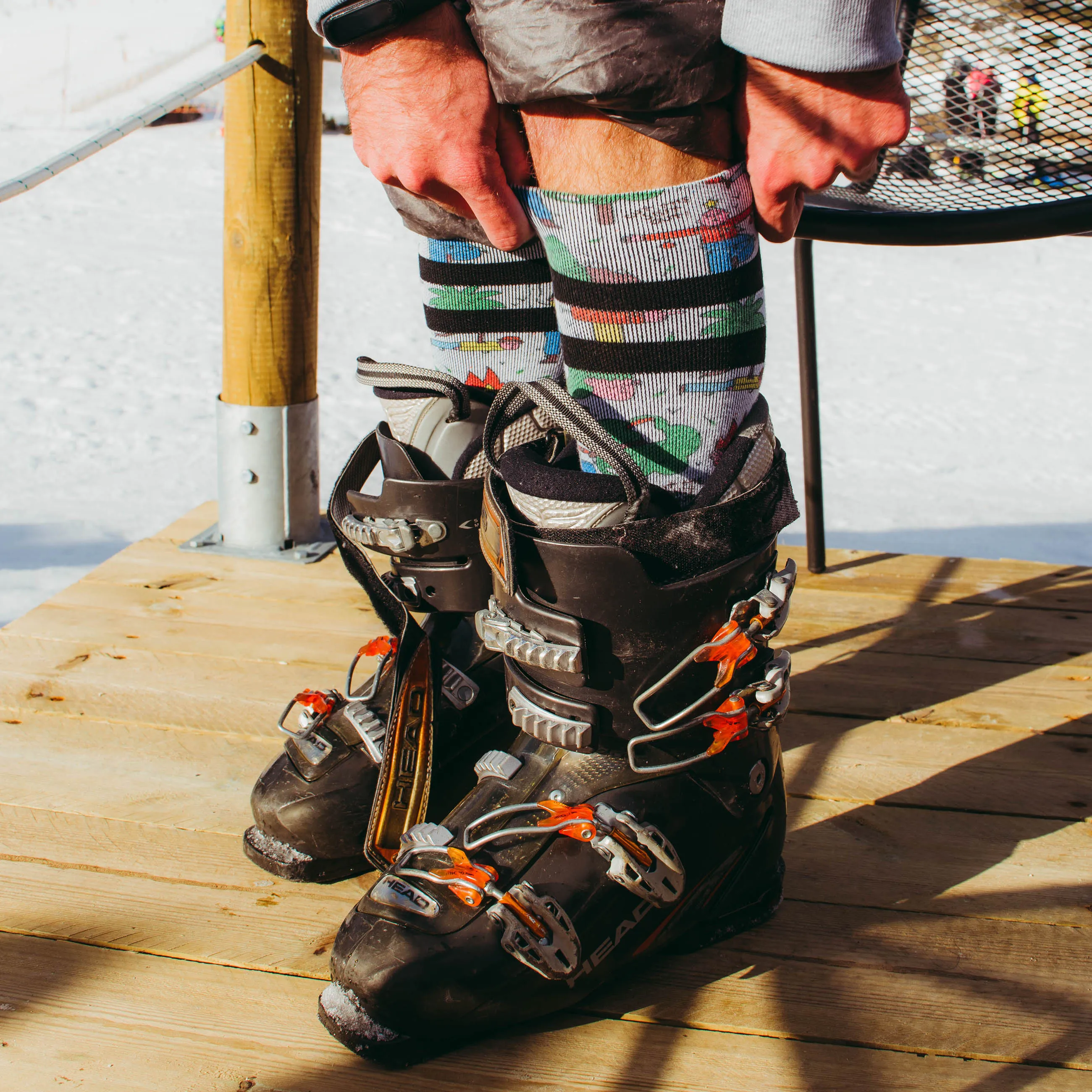 Nahaufnahme von Snow Socks mit buntem Muster und Skischuhen auf Holzbrett im Schnee.