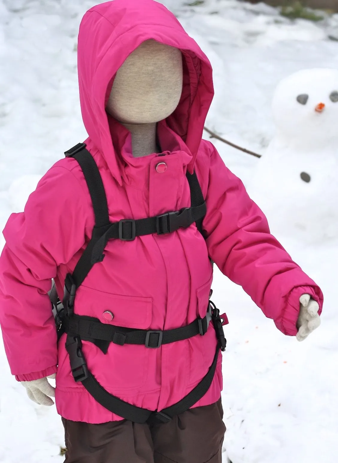 Puppe trägt pinke Winterjacke mit Lil' Ripper Gripper Skilernhilfe im Schnee, im Hintergrund ein Schneemann.