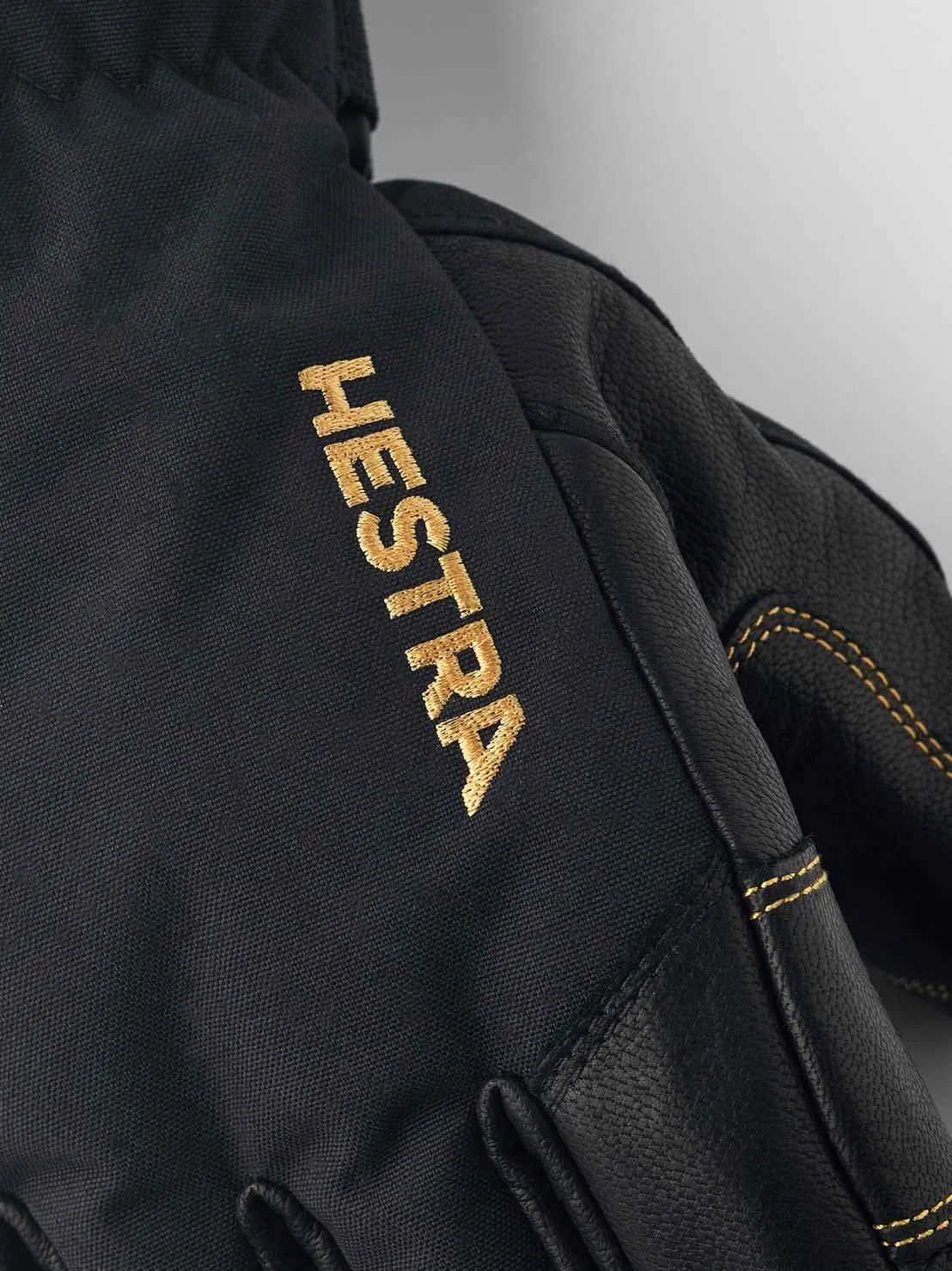 Nahaufnahme eines schwarzen Hestra Gore-Tex Fünffinger-Handschuhs mit goldfarbenem Hestra-Logo.