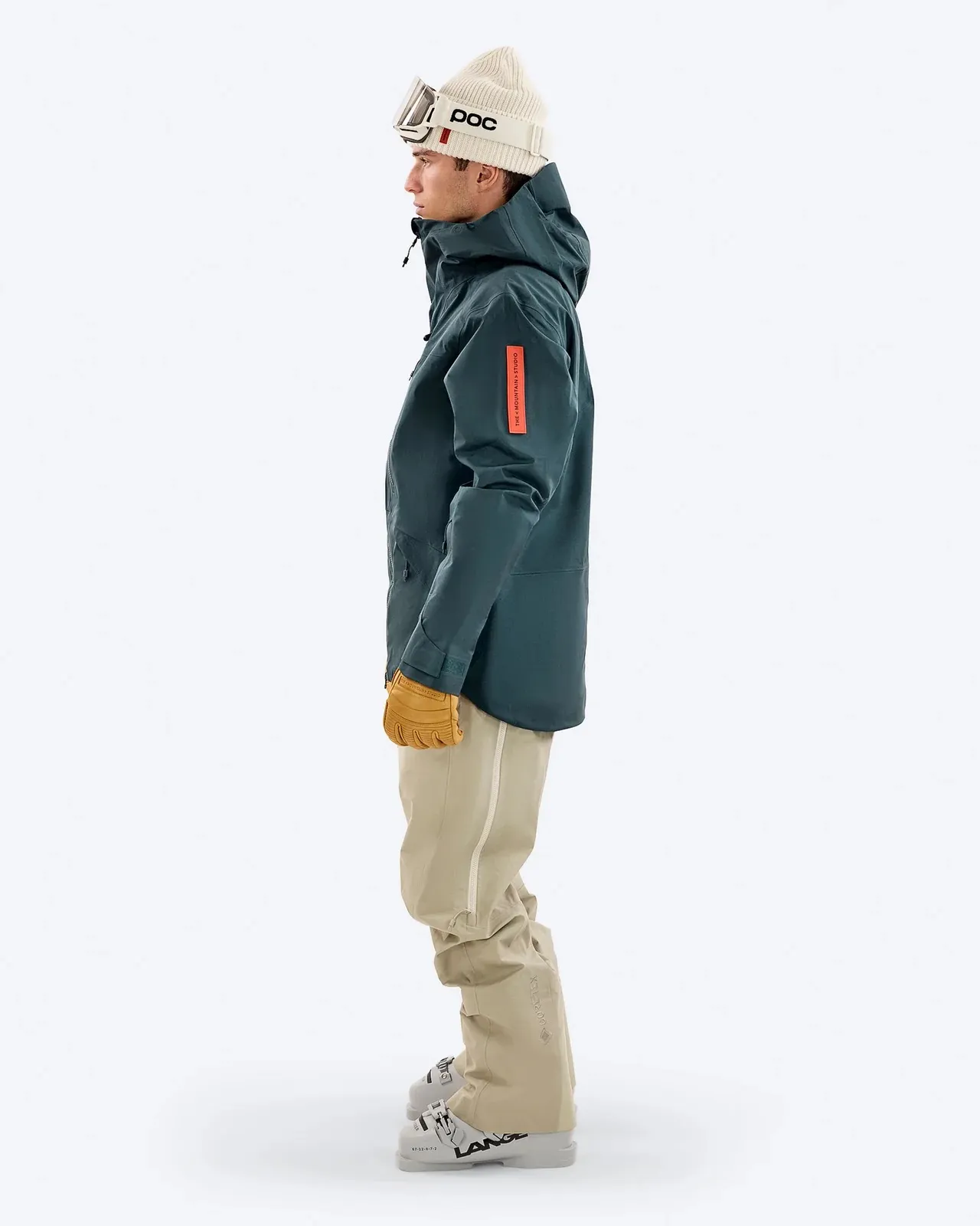 Mann in Winterkleidung in Seitenansicht, mit Skibrille, Mütze und Handschuhen. Er trägt eine blaue Jacke und beigefarbene Hose.