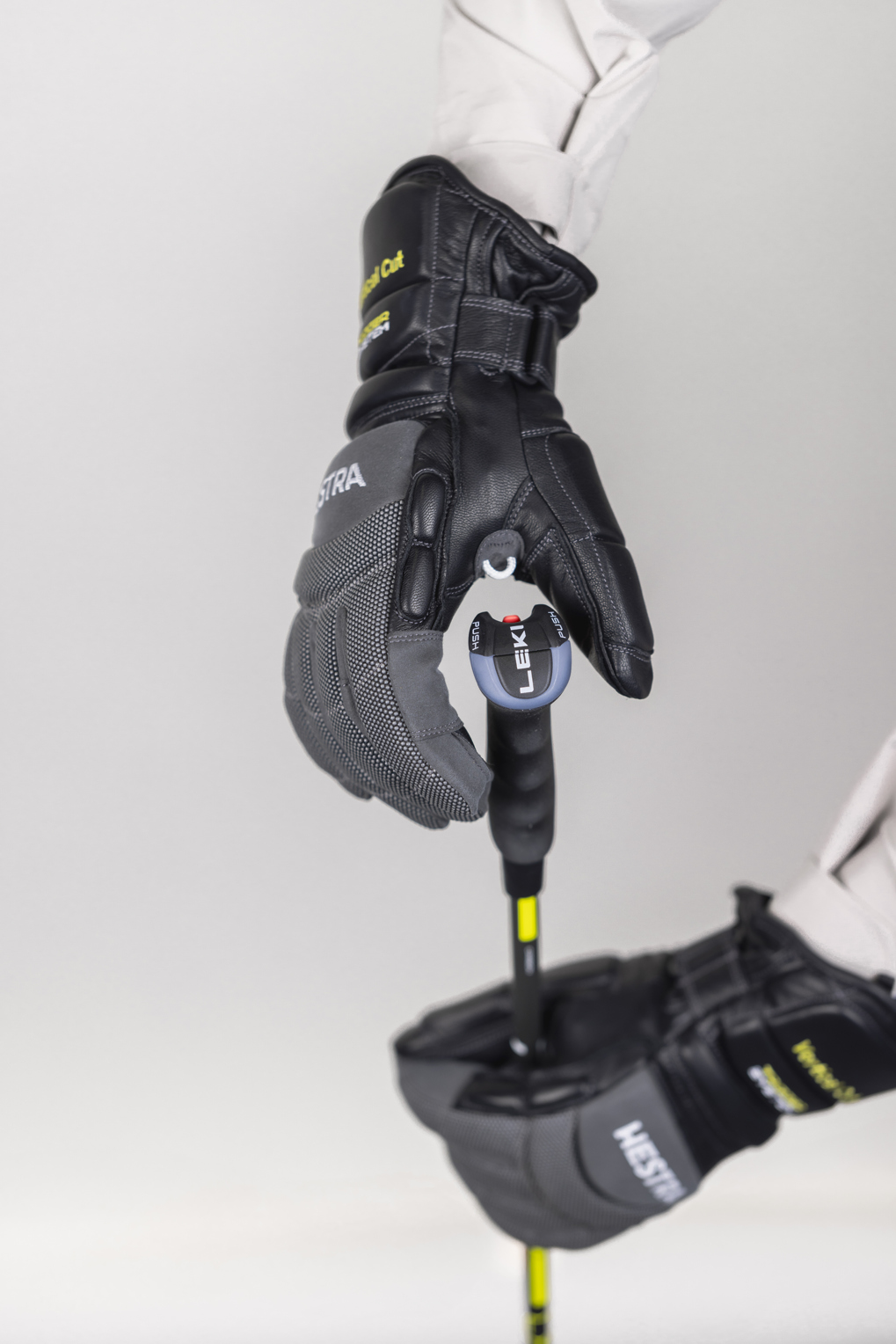 Skihandschuh mit Skistock Eine Hand in einem grauen und schwarzen Hestra Skihandschuh hält einen Leki Skistock. Der Handschuh ist mit einem Auslösemechanismus am Stock befestigt.