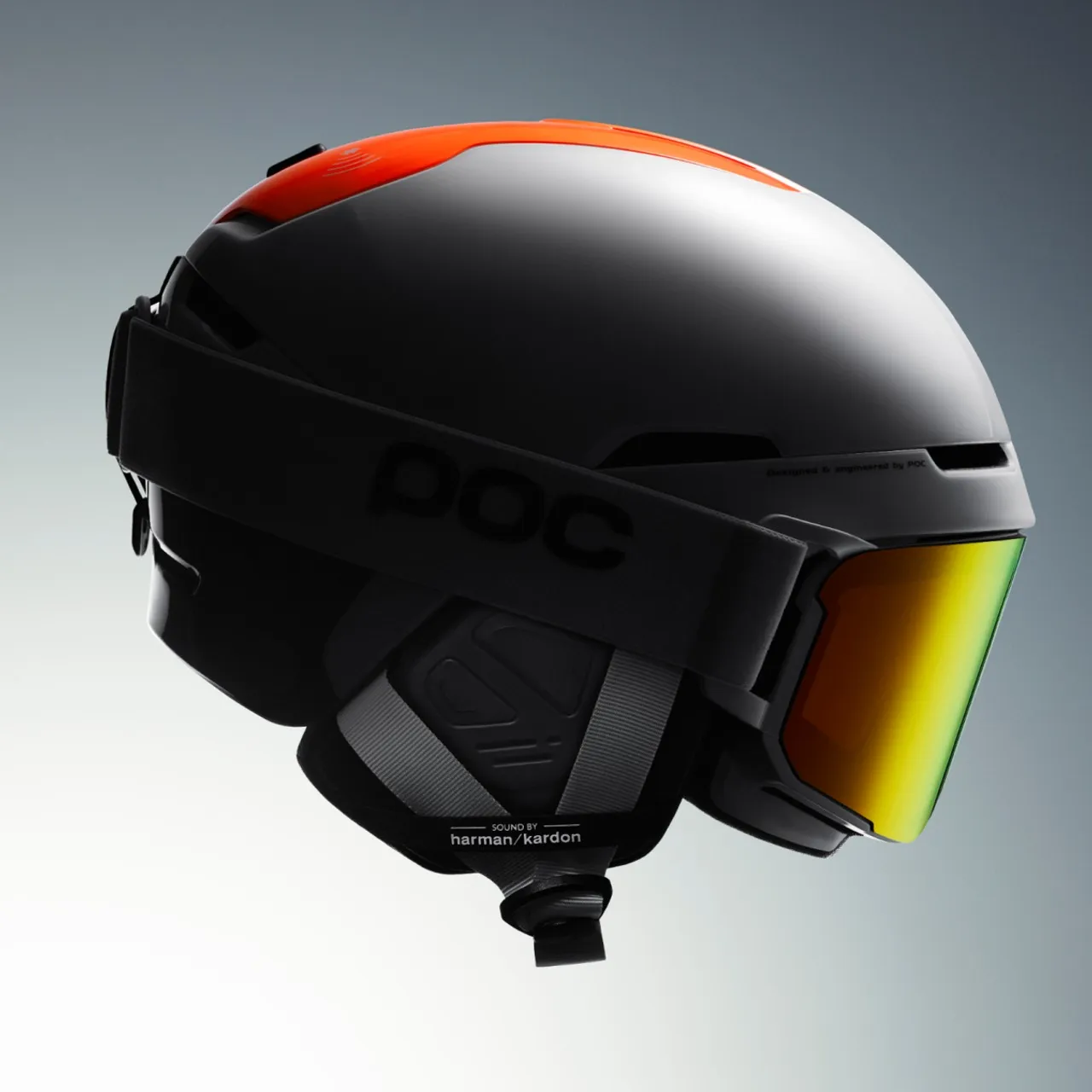 Grauer Skihelm mit orangefarbenem Akzent, schwarzem Brillenband und gelb-goldener Linse, seitliche Ansicht.