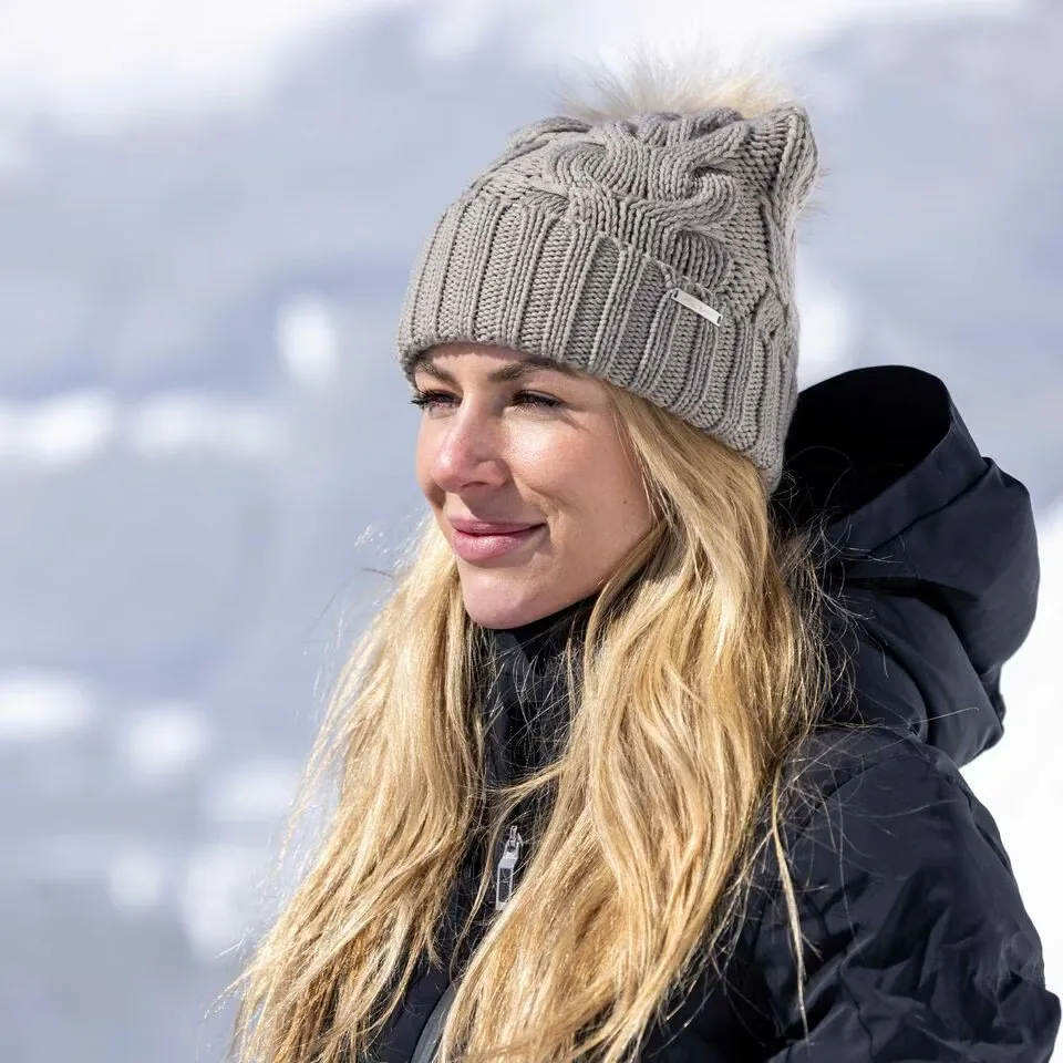 Porträt einer Frau mit blonden Haaren und grauer Strickmütze vor verschneitem Hintergrund.