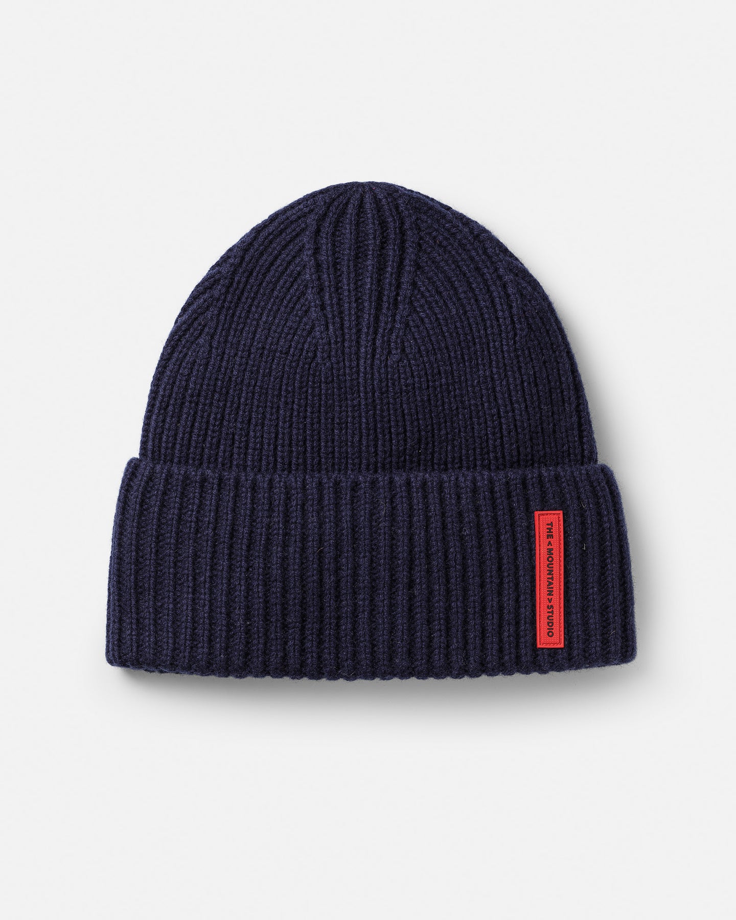 Eine dunkelblaue, gerippte Wollmütze liegt auf einem weißen Untergrund. An der Mütze ist ein rotes Etikett angebracht.