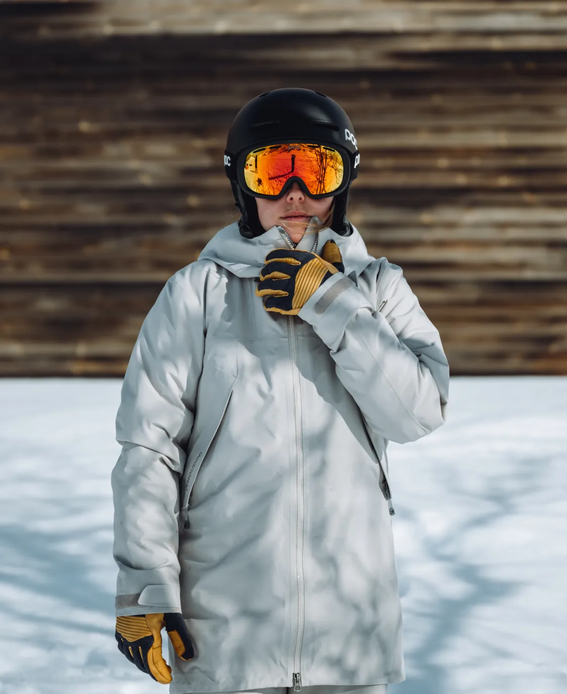 Person mit Fornix Mips Skihelm in Schwarz und orangefarbener Brille, Winterbekleidung und Handschuhen im Schnee.
