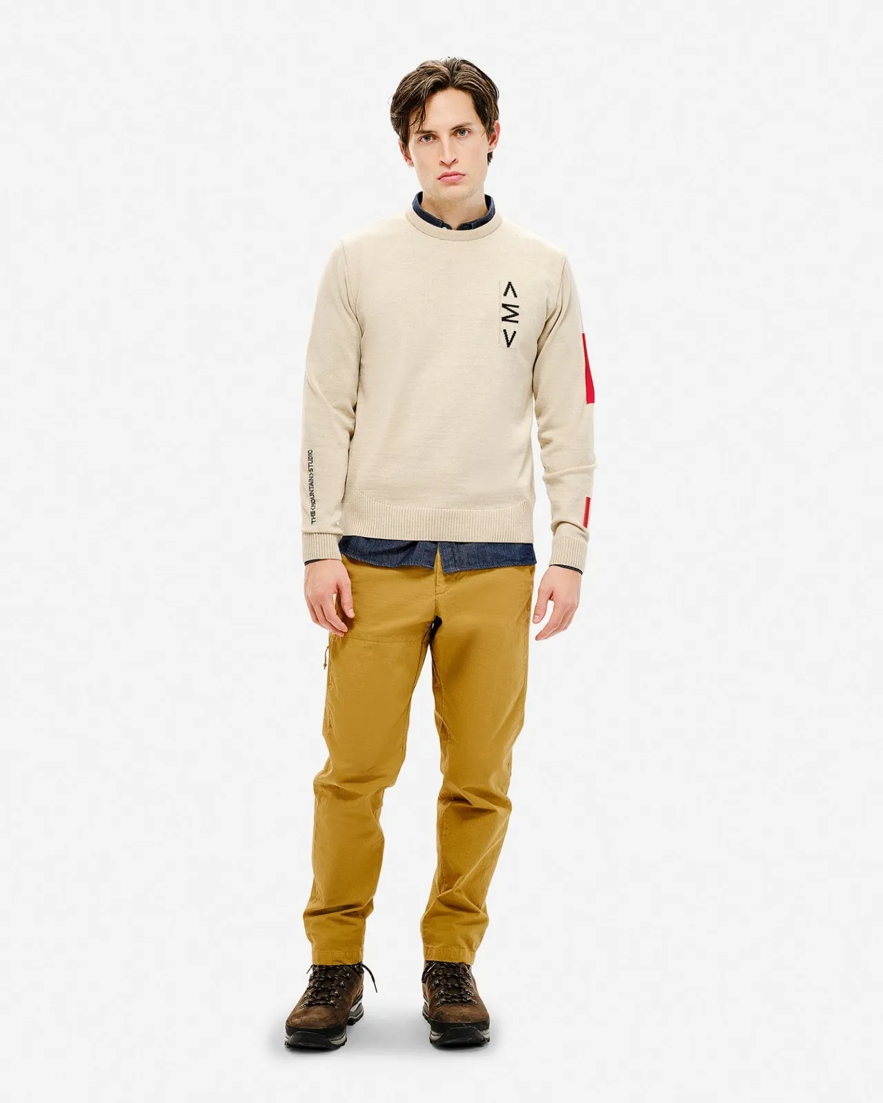 Mann trägt beigen Ski Sweater mit Muster, braune Hose und Schuhe vor einem weißen Hintergrund.