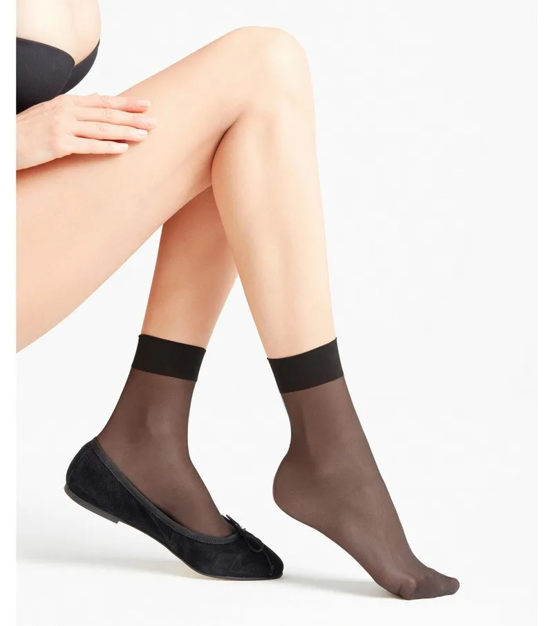 Beine mit schwarzen, transparenten 15 DEN Söckchen und Ballerinas vor weißem Hintergrund.