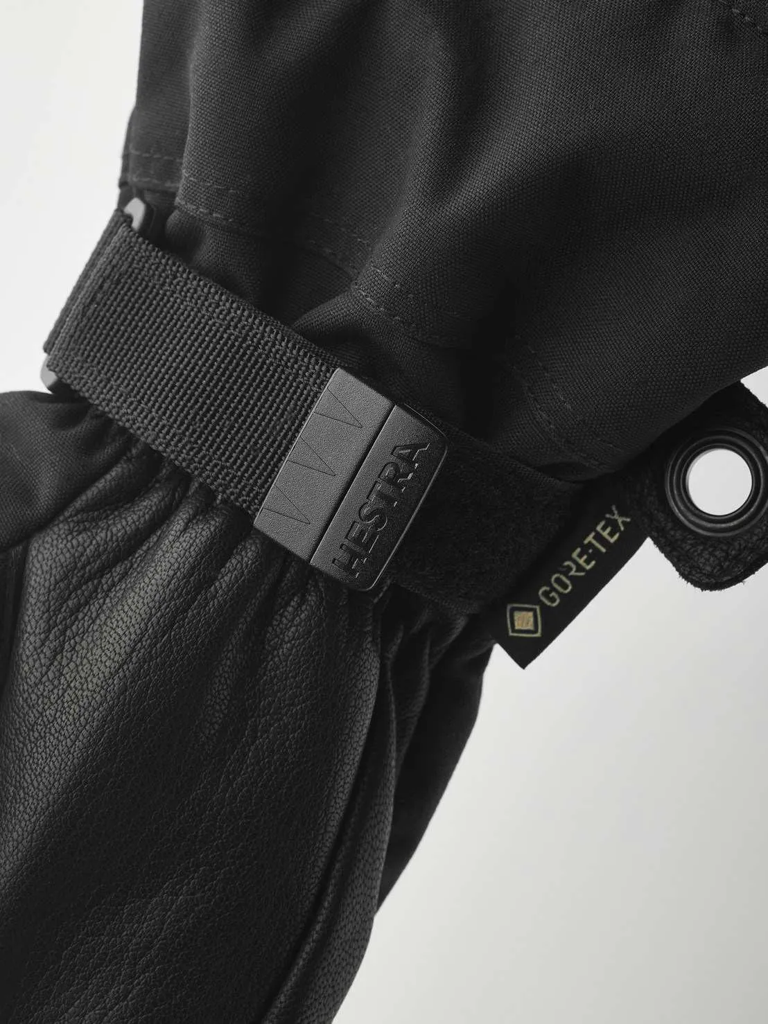 Nahaufnahme eines schwarzen Hestra-Handschuhs mit Gore-Tex-Etikett und verstellbarem Riemen. Das Material ist Leder und Textil.